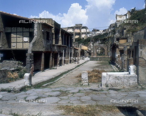 AGC-F-000232-0000 - The decumanus Maximus in Herculaneum. On the left is a large sidewalk and two-story buildings. On the right the columns and remains of buildings. In the background a brick arch - Date of photography: 1989 - Reproduced with the permission of Ministero della Cultura / Alinari Archives, Florence