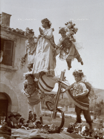 BAQ-F-001356-0000 - "Tableaux vivants" di soggetto religioso portato in processione lungo una strada di un paese. Una giovane donna nelle vesti della vergine Maria, viene sollevata dal suolo, con i piedi appoggiati sul globo terrestre e sulla luna. - Data dello scatto: 1900 ca - Archivi Alinari, Firenze