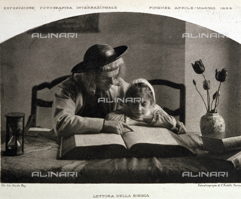 BFB-S-000899-0168 - A man helping a little girl to read the Bible: the pupil follows the text indicated by the teacher's finger. The two figures are sitting leaning on a table on which there are some books, an hourglass and a vase with a few tulips - Date of photography: 1899 ca. - Alinari Archives, Florence