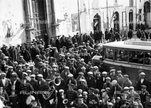 CAD-S-420006-0009 - Musical band and crowd at Piana dei Greci (today Piana degli Albanesi). On the left the portal of the church of Santa Maria Odigitria. On the right a coach with the word "Sciacca" - Date of photography: 09-15/11/1929 - Alinari Archives, Florence