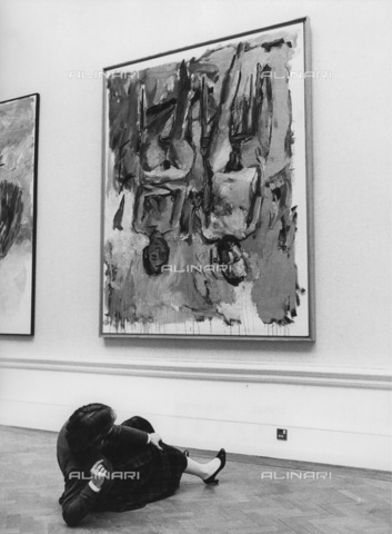 IMA-F-649761-0000 - Una donna distesa sul pavimento mentre guarda il dipinto "Famiglia" di Georg Baselitz (1938-) appeso a testa in giù in modo da incuriosire i visitatori, Royal Academy, Piccadilly, Londra - Data dello scatto: 1981 - Votava / brandstaetter images /Archivi Alinari