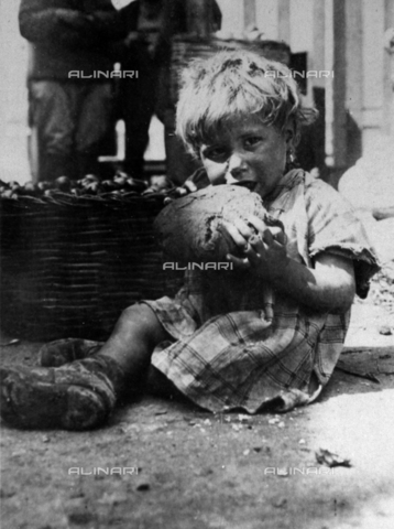 MLD-F-000116-0000 - Ritratto di bambina. La bimba, sporca e malvestita, è ritratta seduta per terra mentre sta mangiando un grosso pezzo di pane - Data dello scatto: 1910-1920 ca. - Archivi Alinari, Firenze